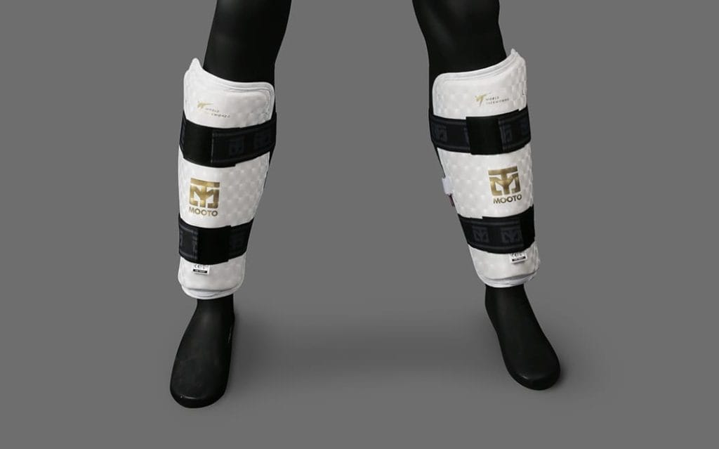 Espinilleras blancas Mooto homologadas por World Taekwondo ajustadas con velcro, un ejemplo de equipamiento de artes marciales bien cuidado.