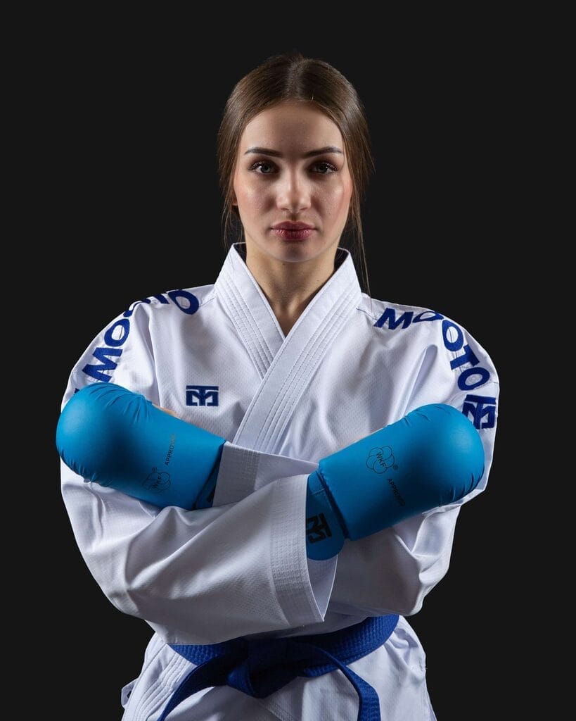 Mujer practicante de karate con karategui blanco Mooto y guantillas azules WKF en perfecto estado de conservación cruzando los brazos.